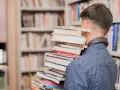 Mężczyzna w bibliotece niesie stos książek, jakby szukał streszczenia "Nad Niemnem".