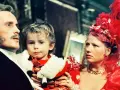 Rodzina w bogatych strojach, ojciec trzyma dziecko. Scena z filmu "Ziemia obiecana", streszczenie ukazuje losy bohaterów.