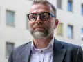 Jacek Bartosiak w okularach i garniturze, na tle budynku z oknami. Jego książki inspirują do refleksji.