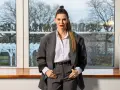 Małgorzata Oliwia Sobczak w garniturze, z włosami spiętymi w kucyk. Za nią okno z widokiem na drzewa, jakby szukała inspiracji do kolejnych książek.