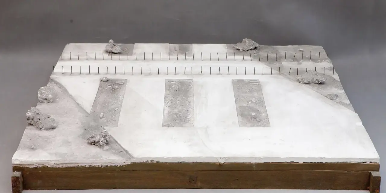 Miniatura terenu przy torze kolejowym z betonowymi płytami i kamieniami.