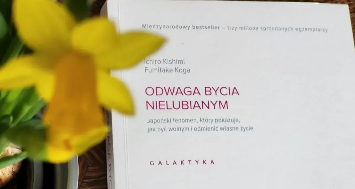 Żółty narcyz obok książki "Odwaga bycia nielubianym". Autorzy pokazują, jak odnaleźć wolność i odmienić życie.