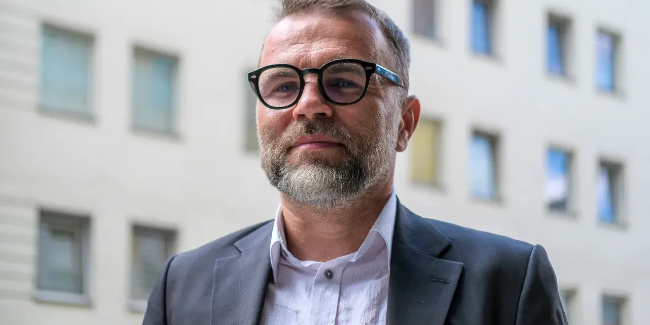 Jacek Bartosiak w okularach i garniturze, na tle budynku z oknami. Jego książki inspirują do refleksji.