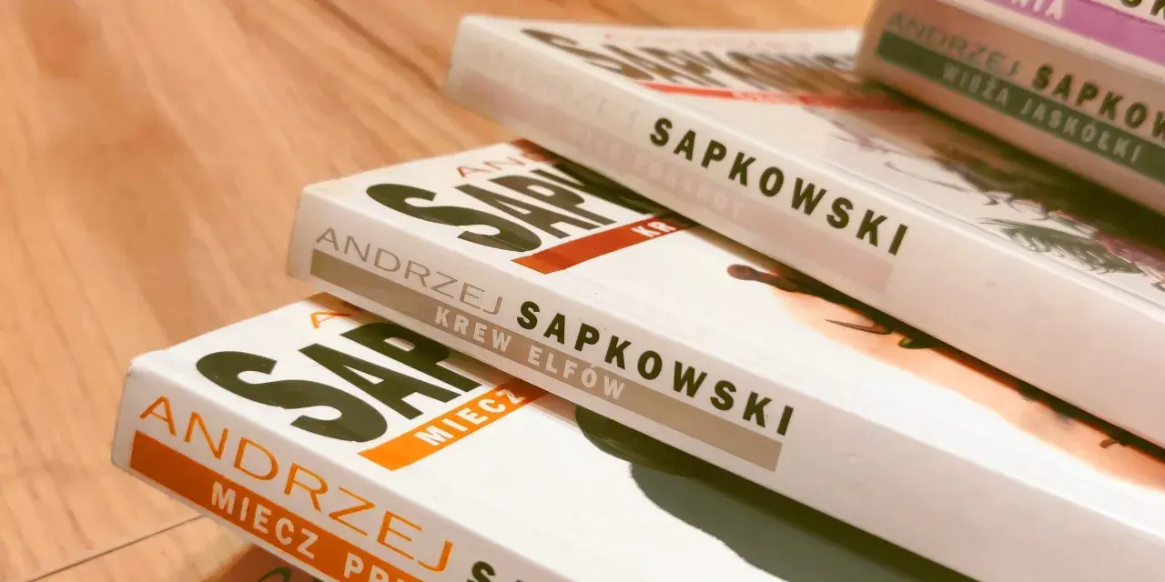 Stos książek Andrzeja Sapkowskiego, w tym "Krew Elfów" i "Miecz Przeznaczenia", gotowy do podróży po świecie Wiedźmina.