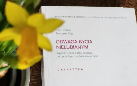 Żółty narcyz obok książki "Odwaga bycia nielubianym". Autorzy pokazują, jak odnaleźć wolność i odmienić życie.