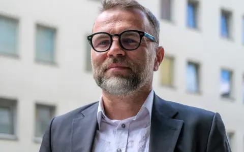Jacek Bartosiak w okularach i garniturze, na tle budynku z oknami. Jego książki inspirują do refleksji.
