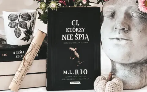 Książka "Ci, którzy nie śpią" M.L. Rio, obok kubka i ozdobnej głowy. Nawet jeśli jesteśmy złoczyńcami, warto po nią sięgnąć.