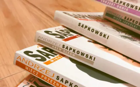Stos książek Andrzeja Sapkowskiego, w tym "Krew Elfów" i "Miecz Przeznaczenia", gotowy do podróży po świecie Wiedźmina.