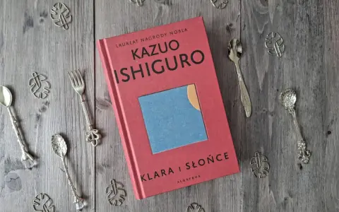 Książka "Klara i Słońce" Kazuo Ishiguro na drewnianym tle, otoczona ozdobnymi łyżeczkami i listkami.