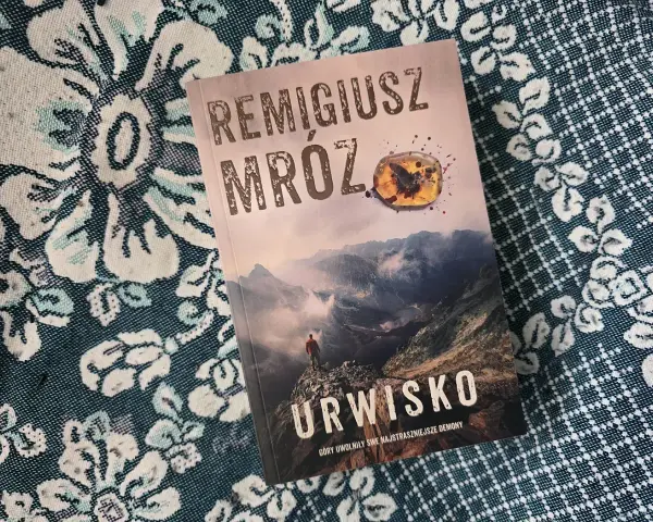 Okładka najnowszej książki Remigiusza Mroza "Urwisko". Góry, mgła i samotna postać na szczycie.