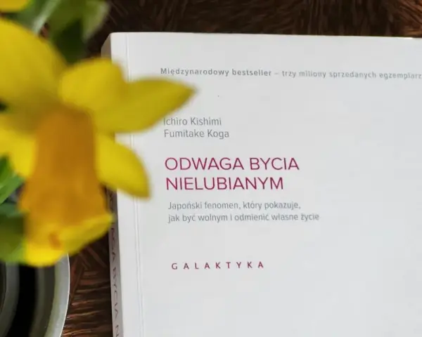 Żółty narcyz obok książki "Odwaga bycia nielubianym". Autorzy pokazują, jak odnaleźć wolność i odmienić życie.
