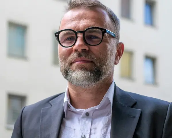 Jacek Bartosiak w okularach i garniturze, na tle budynku z oknami. Jego książki inspirują do refleksji.