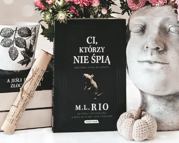 Książka "Ci, którzy nie śpią" M.L. Rio, obok kubka i ozdobnej głowy. Nawet jeśli jesteśmy złoczyńcami, warto po nią sięgnąć.