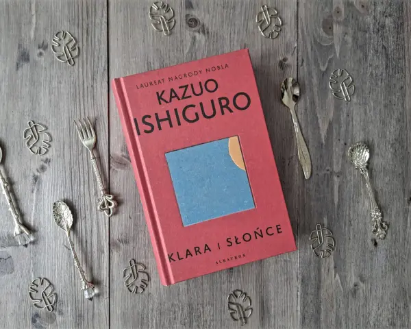 Książka "Klara i Słońce" Kazuo Ishiguro na drewnianym tle, otoczona ozdobnymi łyżeczkami i listkami.