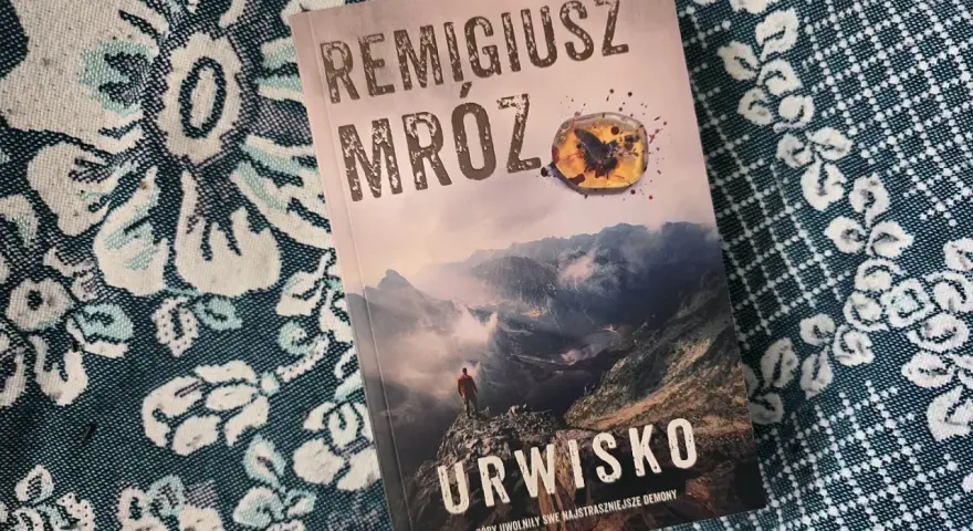 Okładka najnowszej książki Remigiusza Mroza "Urwisko". Góry, mgła i samotna postać na szczycie.