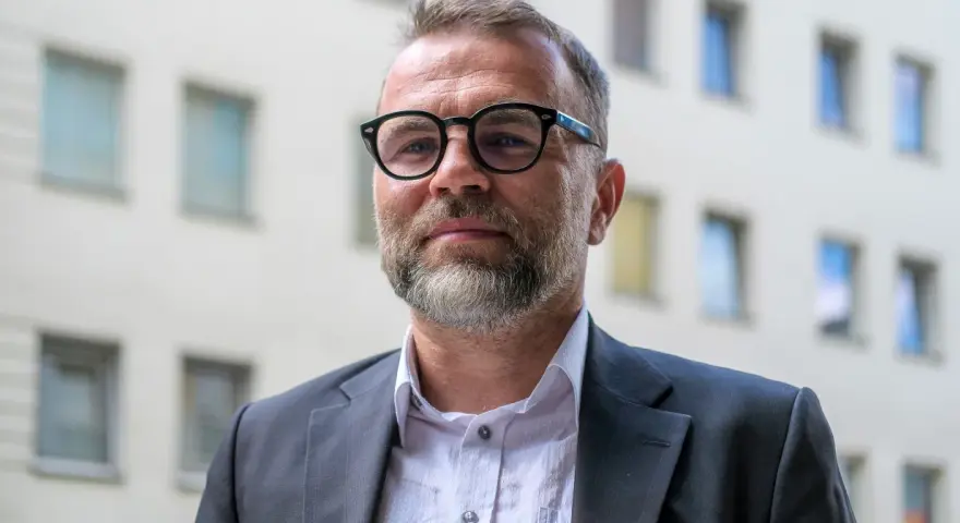 Jacek Bartosiak w okularach i garniturze, na tle budynku z oknami. Jego książki inspirują do refleksji.