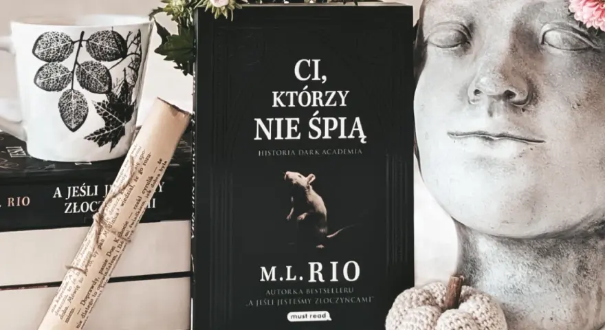 Książka "Ci, którzy nie śpią" M.L. Rio, obok kubka i ozdobnej głowy. Nawet jeśli jesteśmy złoczyńcami, warto po nią sięgnąć.