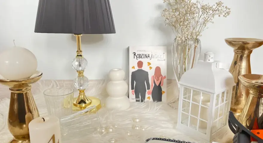 Książka "Rodzina Monet. Diament" wśród świec, złotych świeczników i ozdób.
