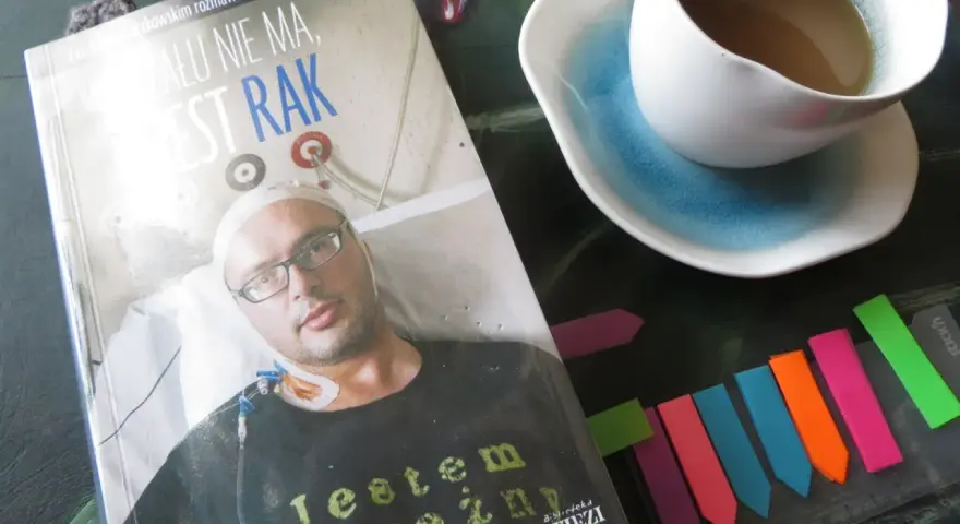 Książka "Żalu nie ma, jest rak" z wizerunkiem autora, obok filiżanka kawy i kolorowe zakładki.