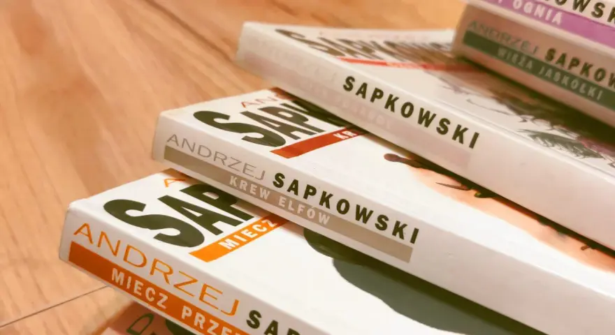 Stos książek Andrzeja Sapkowskiego, w tym "Krew Elfów" i "Miecz Przeznaczenia", gotowy do podróży po świecie Wiedźmina.