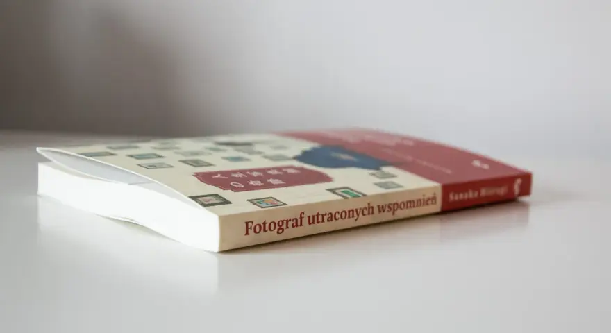 Książka "Fotograf utraconych wspomnień" z japońskimi znakami na okładce, leżąca na białym blacie.