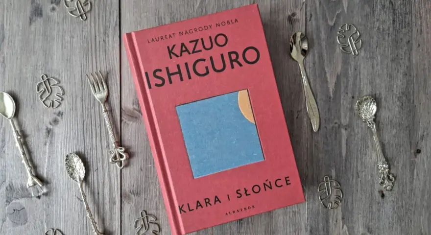 Książka "Klara i Słońce" Kazuo Ishiguro na drewnianym tle, otoczona ozdobnymi łyżeczkami i listkami.