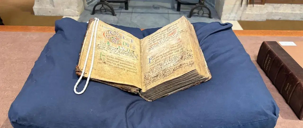Stary manuskrypt, być może panegiryk, z ozdobnymi inicjałami. Obok oprawiony brewiarz.